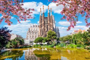 A large building with towers and a pond with trees and a pond with pink flowers. by Chasing the Sun Vacations