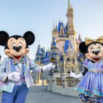 Two mickey and minnie characters standing in front of a castle during a magical all-inclusive vacation. by Chasing the Sun Vacations