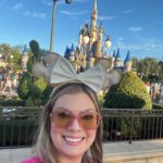 Woman wearing minnie mouse ears taking a selfie at disney with the castle in the background. by Chasing the Sun Vacations